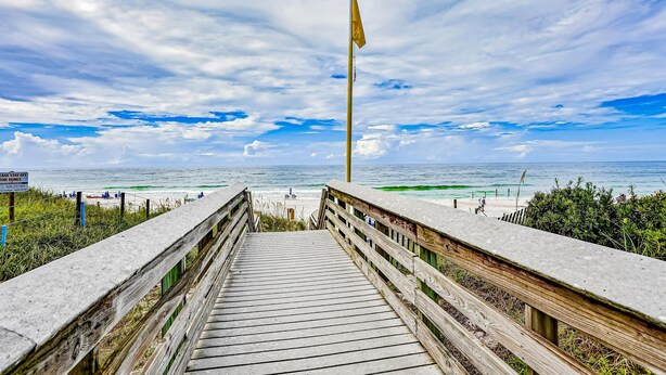 A wooden boardwalk leading to a beach with a flagpole and a sign. - Azure on 30A 1-205- A Wave From it All (Santa Rosa Beach)