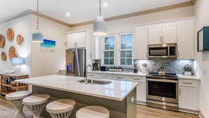 A modern kitchen with white cabinets, stainless steel appliances, and a large island with bar stools. - Azure on 30A 1-205- A Wave From it All (Santa Rosa Beach)