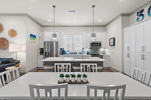 A modern kitchen with white cabinetry, stainless steel appliances, and a central island with seating. - Azure on 30A 1-205- A Wave From it All (Santa Rosa Beach)