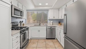 A modern kitchen with white cabinets, stainless steel appliances, and a tiled floor. - @ Marbella Lane - Gem w/ Outdoor Fun Pool & Trails (Palm Springs)