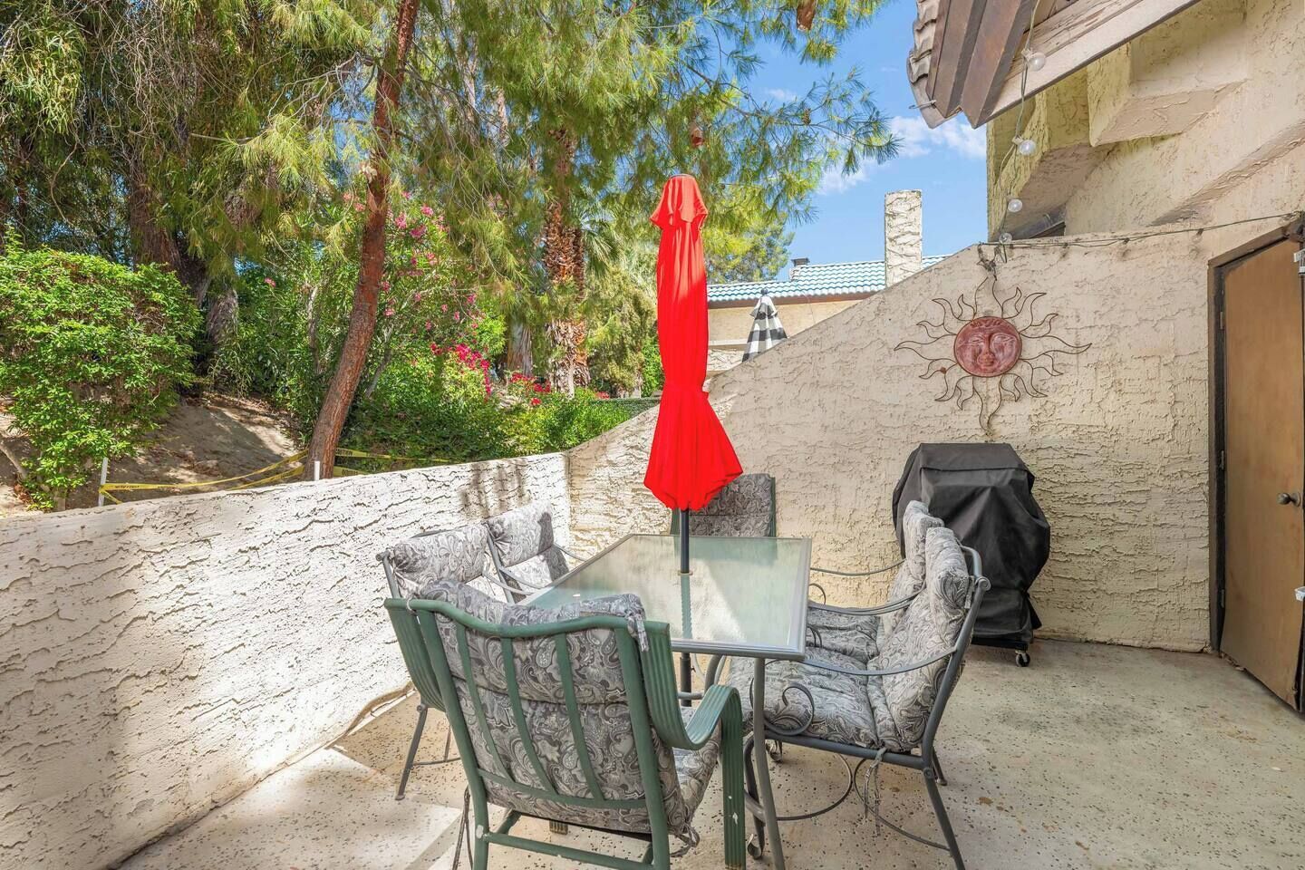 Eine Terrasse im Freien mit Tisch, Stühlen, einem roten Sonnenschirm und einem Grill.