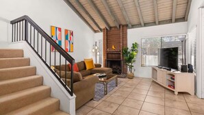 A living room with a staircase, a fireplace, a television, and a bookshelf. - @ Marbella Lane - Gem w/ Outdoor Fun Pool & Trails (Palm Springs)