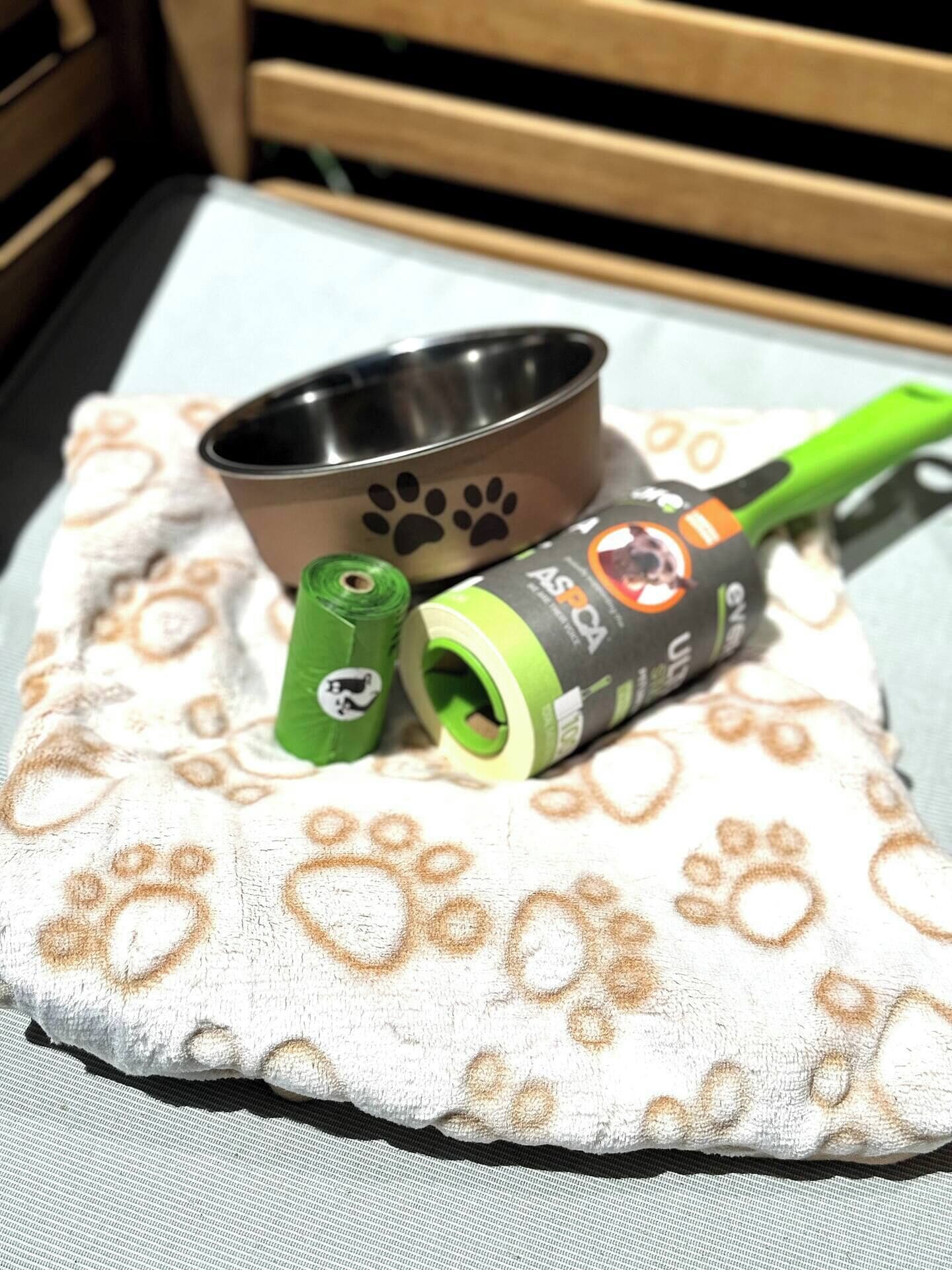 Un panier pour animal de compagnie orné d’un motif représentant des empreintes de pattes, une gamelle en métal et un rouleau de ruban adhésif vert.