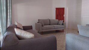 A living room with a grey sofa set, a red door, and a tiled floor.