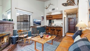 Una sala de estar acogedora con chimenea, muebles de madera y una cocina al fondo.
