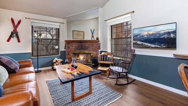 Una sala de estar acogedora con chimenea, sofá de cuero, mesa de comedor de madera y un ventanal con vistas a la montaña.