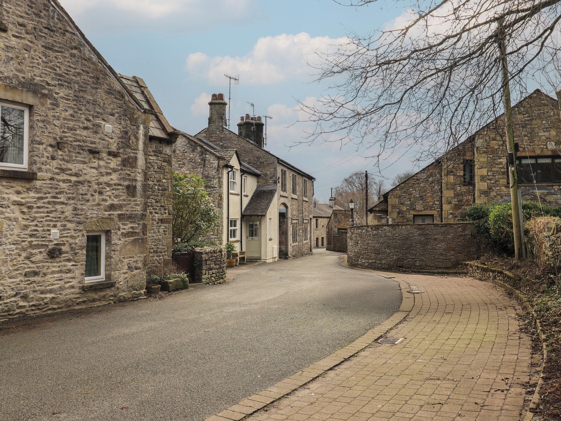 A narrow street lined with stone buildings, a paved sidewalk, and a clear sky.