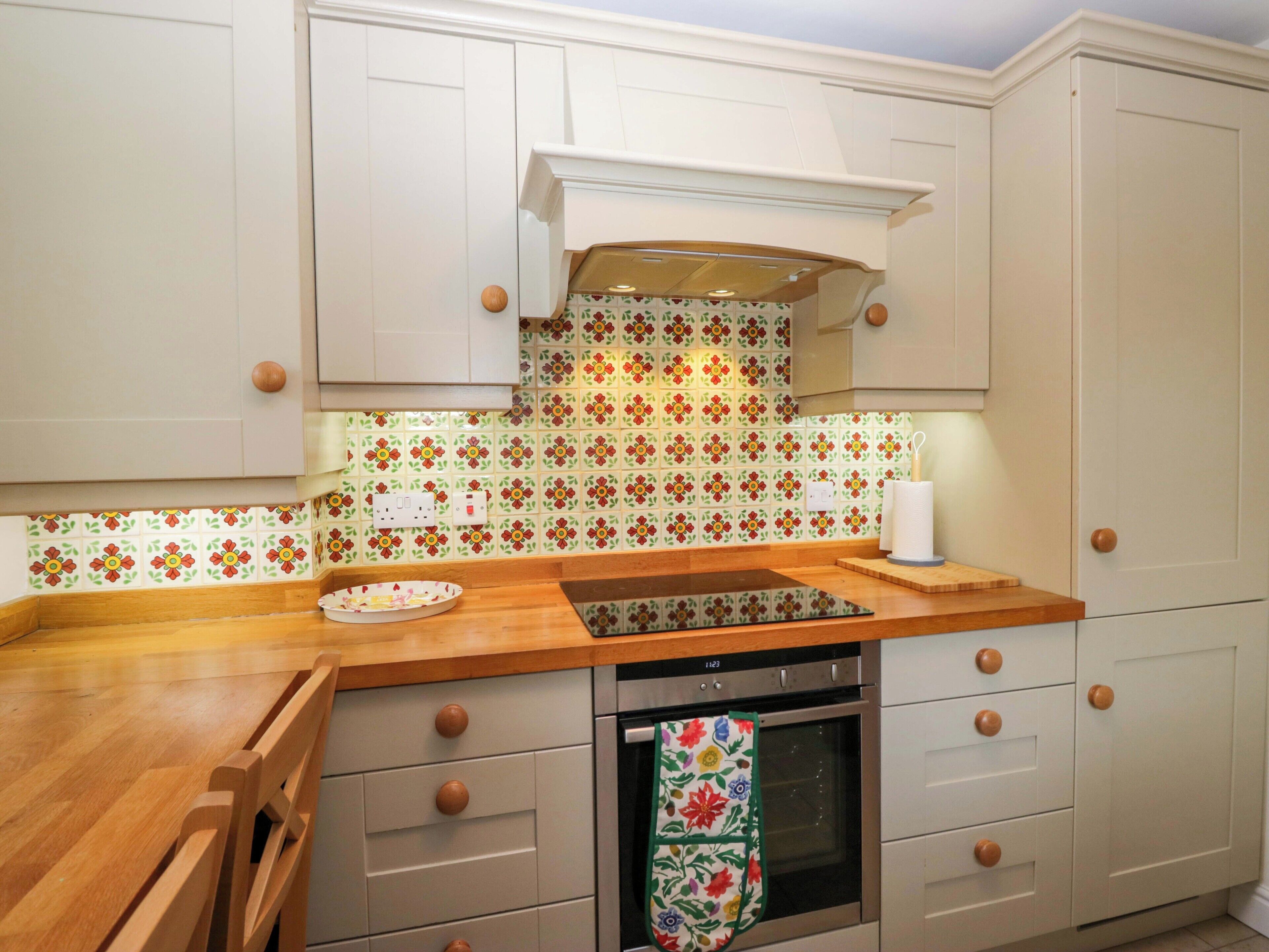 Una cocina con armarios blancos, encimera de madera, estufa y salpicadero con diseño.