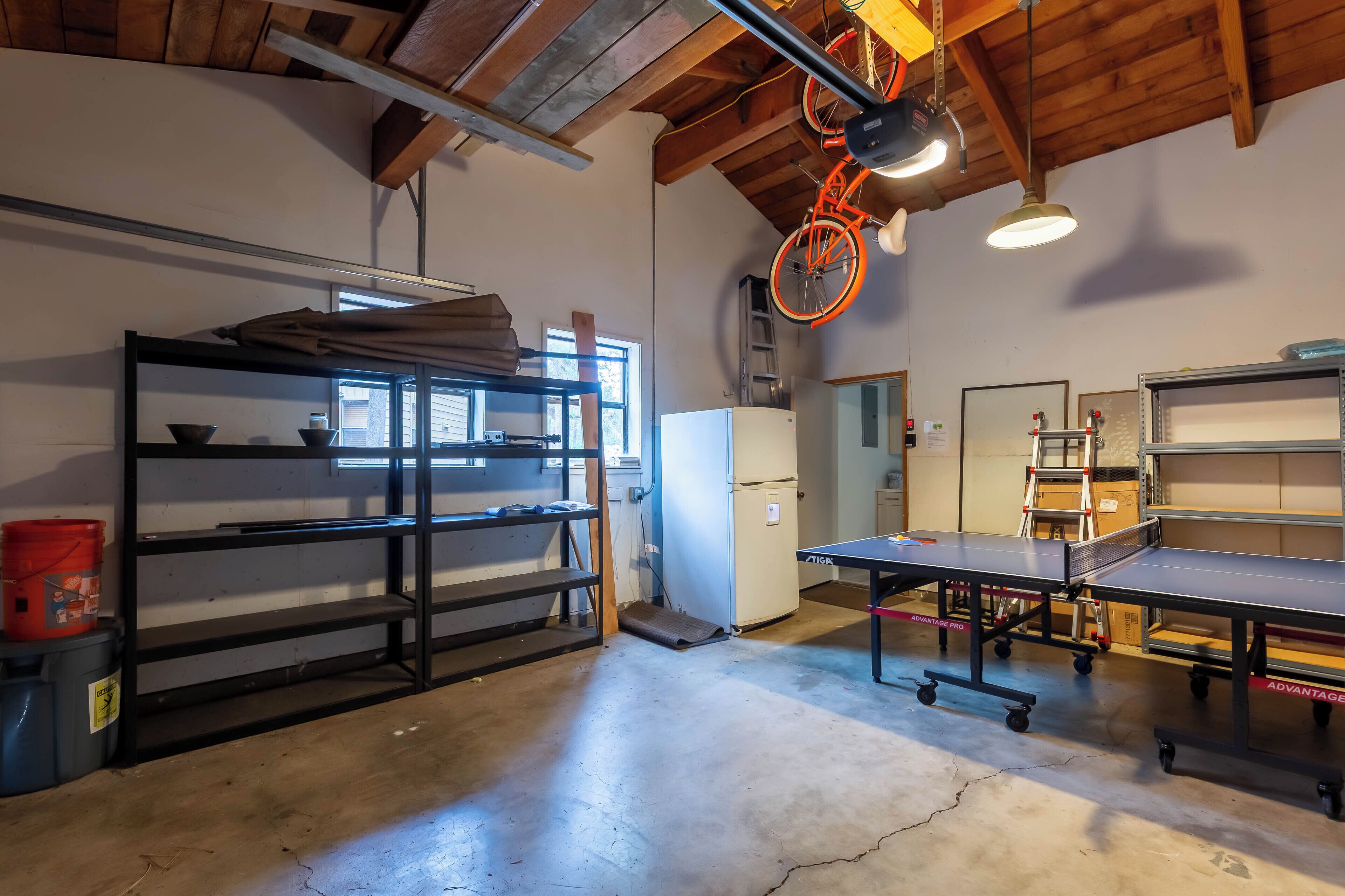 Una habitación amplia con mesa de ping pong, estantes y una bicicleta colgada del techo.