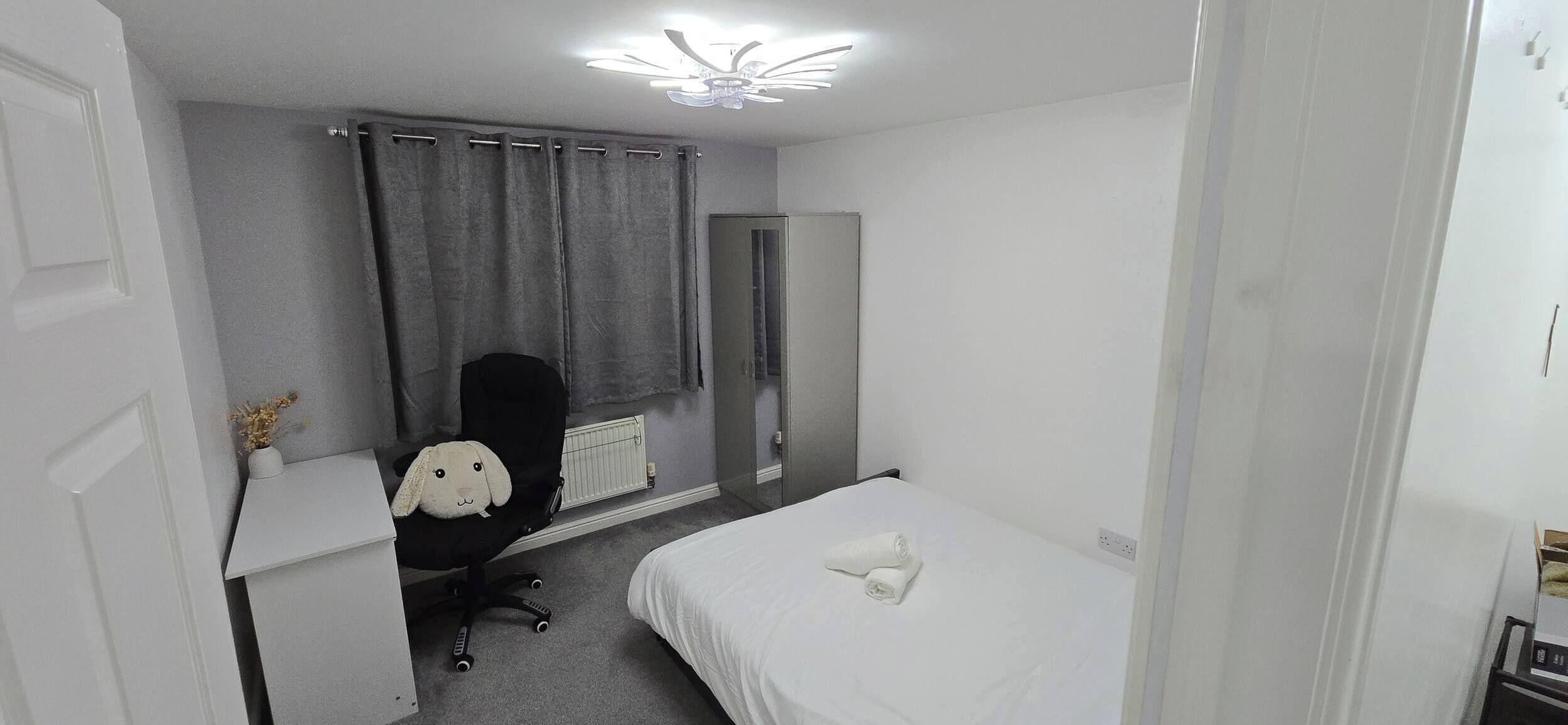 A small, clean room with a bed, a desk, a chair, a radiator, and a ceiling fan.