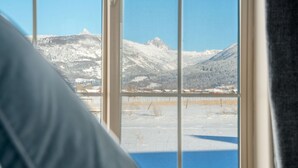 A room with a large window offering a view of snow-covered mountains and a clear blue sky. - Teton Homestead: White Pine w/ Hot Tub & Views (Victor)