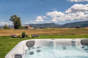 Een bubbelbad met uitzicht op een landelijk landschap, inclusief velden, een huis en bergen.