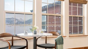 A dining area with a round table, two chairs, and a view of a snowy landscape through large windows with blinds. - Teton Homestead: White Pine w/ Hot Tub & Views (Victor)