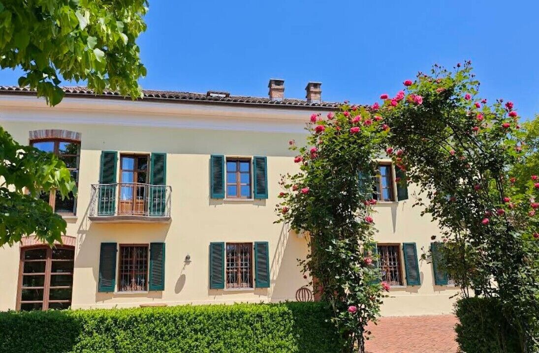 Un bâtiment à deux étages doté d’un balcon au deuxième étage, d’un jardin où fleurissent de magnifiques plantes et d’un ciel bleu azur.