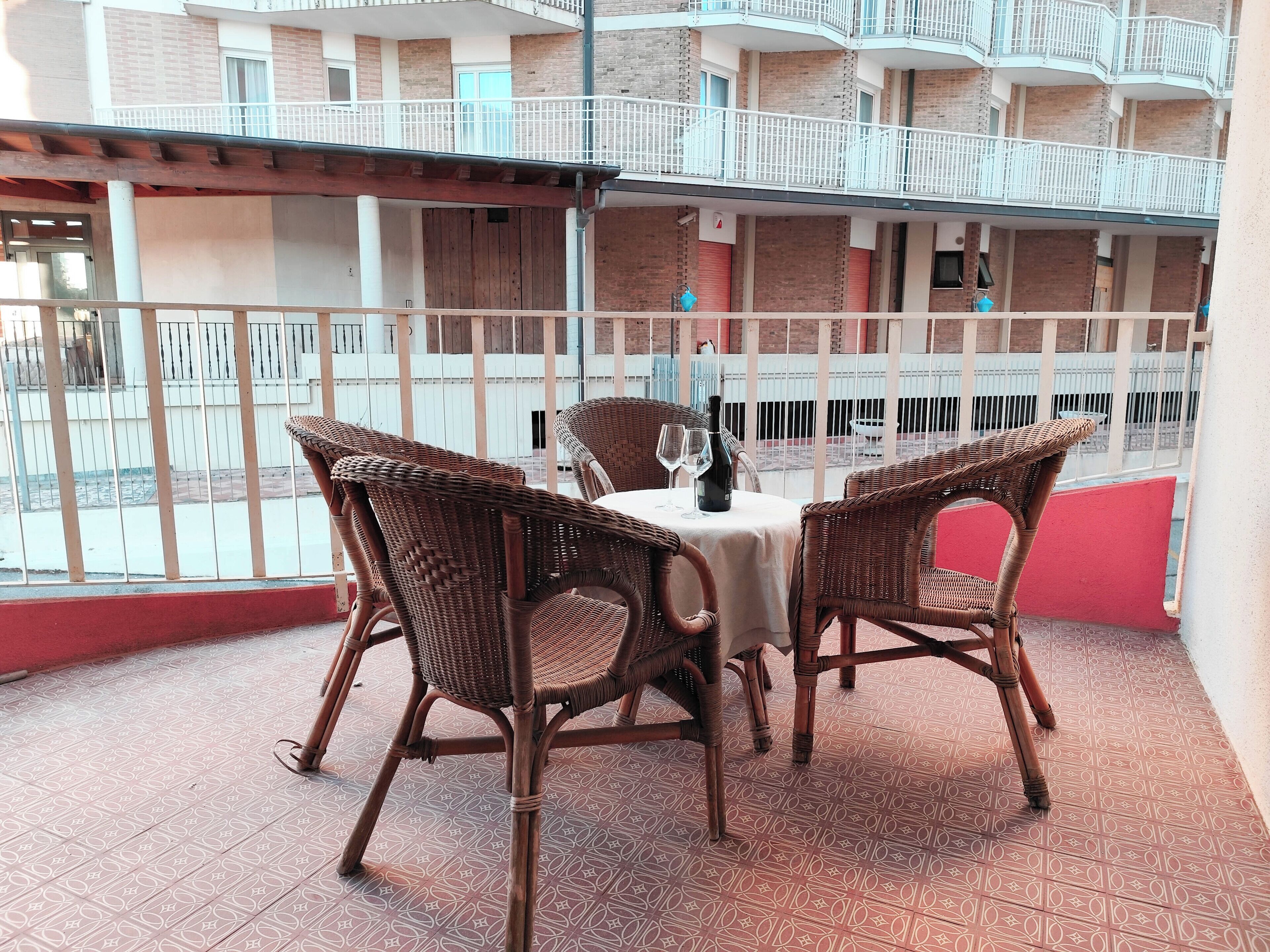 Un balcón con sillones de mimbre, una mesa, una botella y dos vasos.