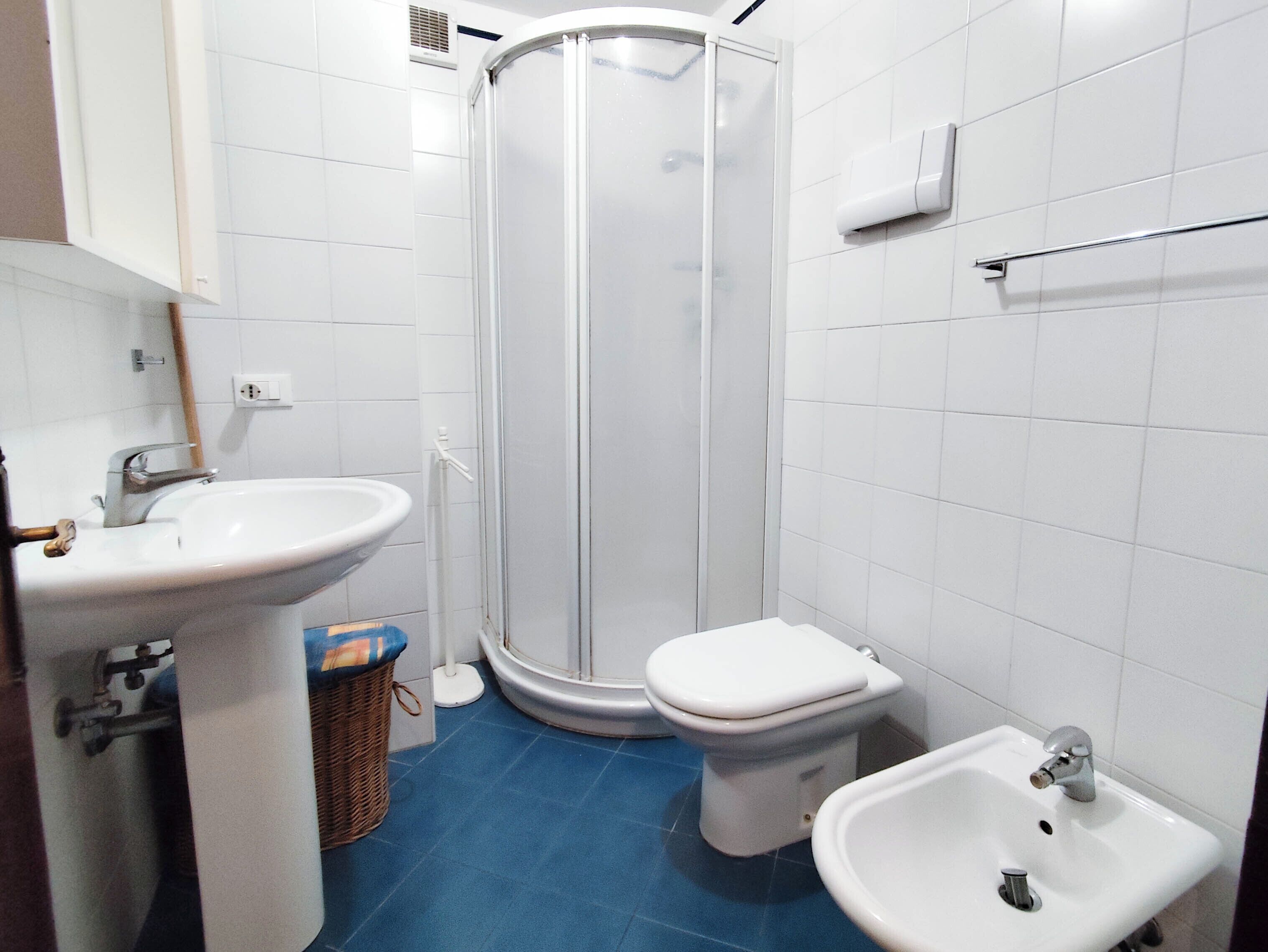 A bathroom with a shower, toilet, sink, and a blue floor.