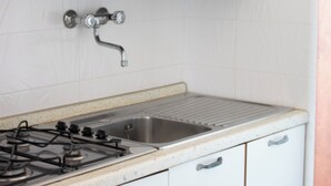 Ett kök med vita skåp, en diskho i rostfritt stål och en gasspis.