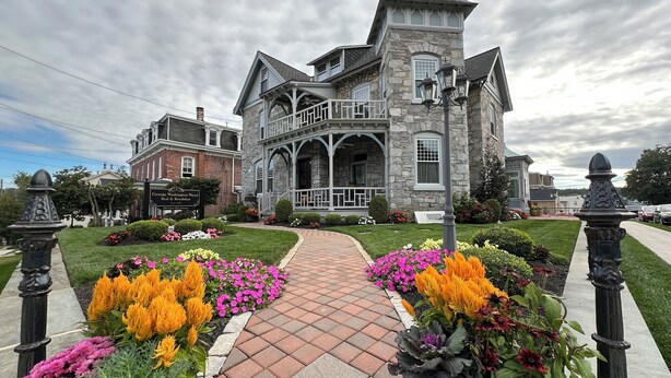 A historic stone building with a prominent tower, a brick building in the background, and a well-maintained garden with colorful flowers and a brick pathway. - Charming Conshohocken B+B Near Philly (Conshohocken)