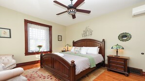A bedroom with a wooden bed, a ceiling fan, a window with lace curtains, a chair, a nightstand with a lamp, and a dresser. - Charming Conshohocken B+B Near Philly (Conshohocken)
