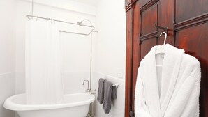 A bathroom with a white bathtub, a shower curtain, a towel rack with towels, and a wooden door. - Charming Conshohocken B+B Near Philly (Conshohocken)