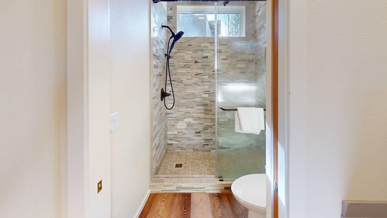Une salle de bain moderne avec une douche à parois de verre, un plancher en bois et des toilettes blanches.