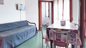 A room with a blue sofa, a table with a floral tablecloth, and a ceiling light. - Bright Holiday Home With Balcony (Jesolo)