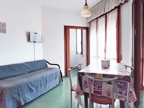 A room with a blue sofa, a table with a floral tablecloth, and a ceiling light. - Bright Holiday Home With Balcony (Jesolo)