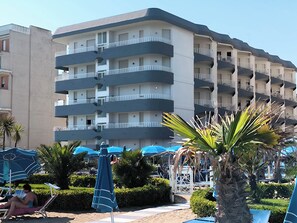 A multi-story hotel with balconies, a pool area with umbrellas, and palm trees. - Bright Holiday Home With Balcony (Jesolo)