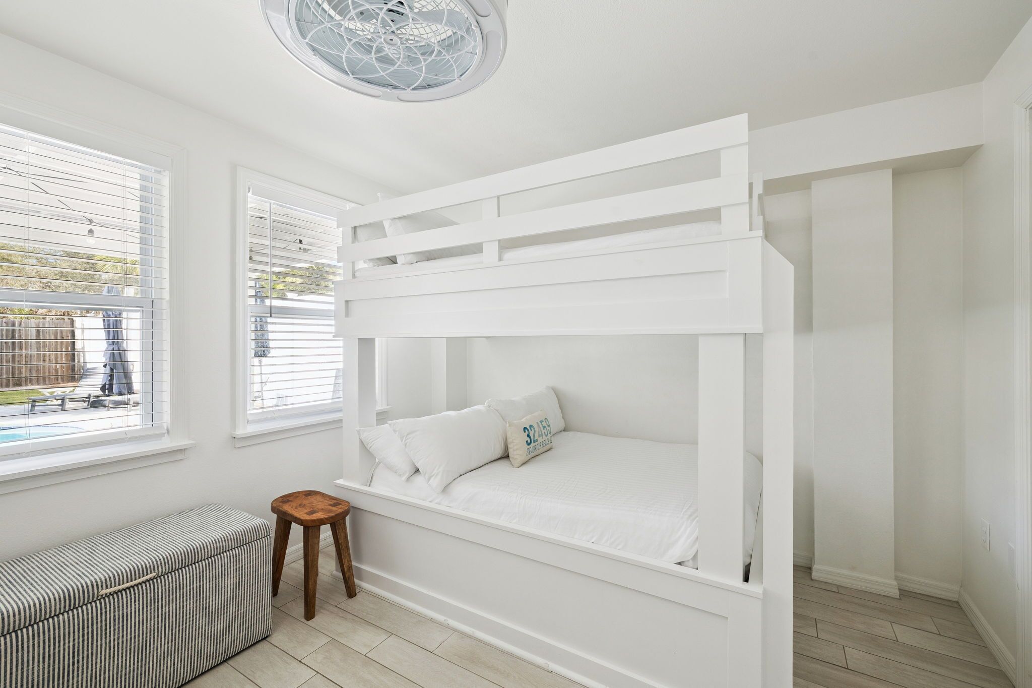Un letto a castello con biancheria e cuscini bianchi, una piccola panca e una ventola a soffitto.