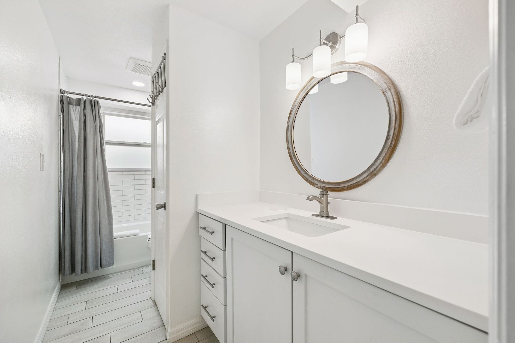 A bathroom with a white vanity, a round mirror with a gold frame, and a shower curtain.