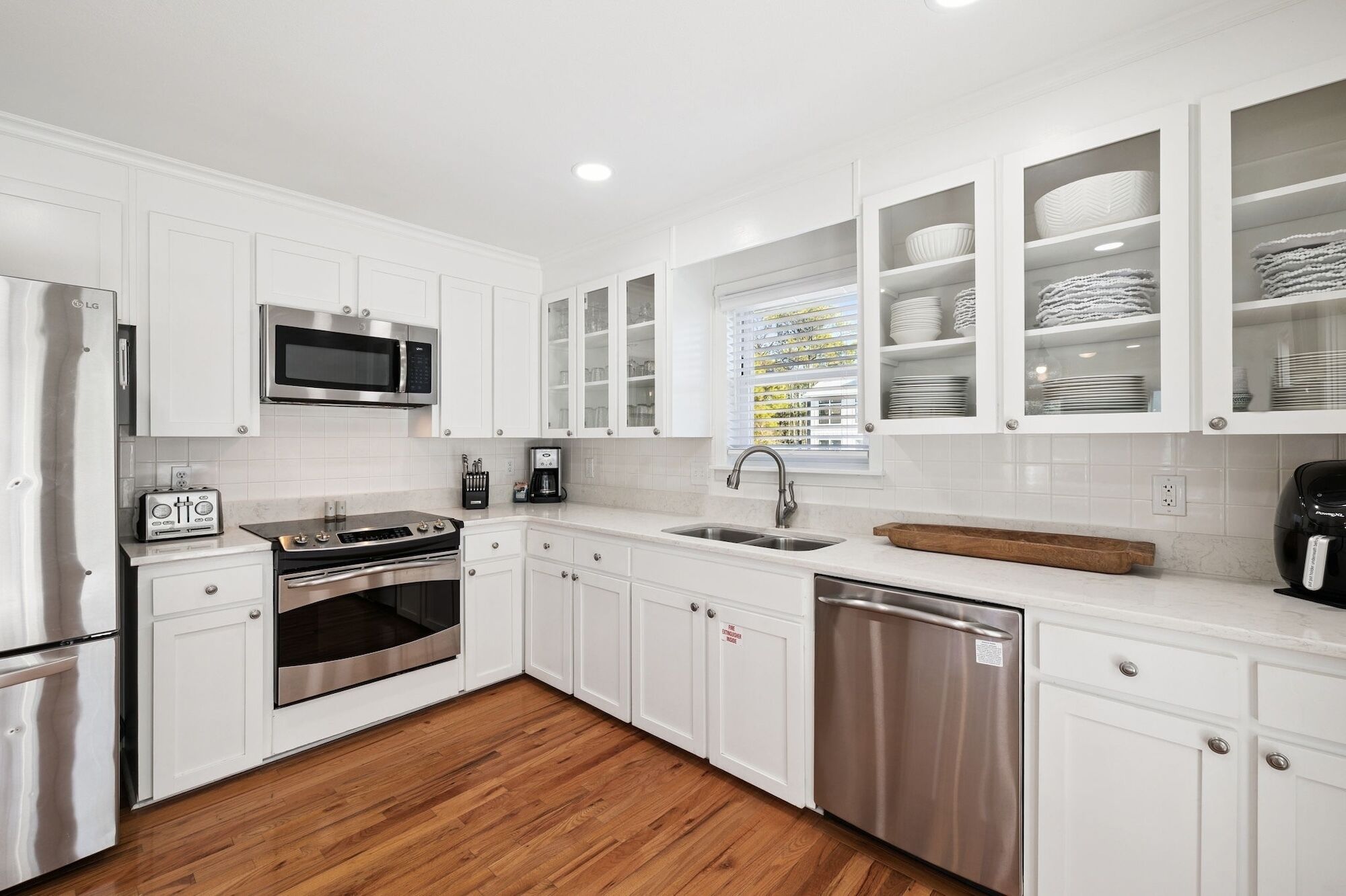 A modern kitchen with white cabinetry, stainless steel appliances, and a wooden floor.