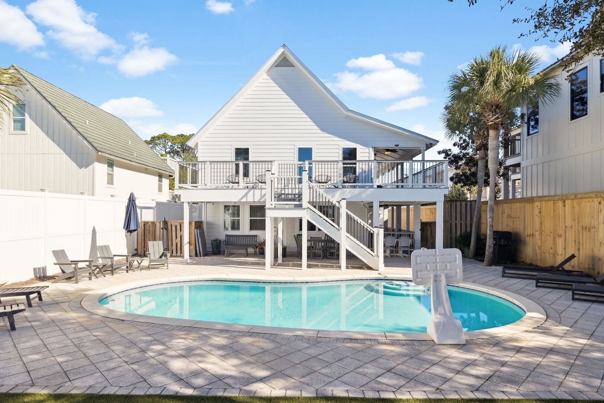 A two-story house with a pool, outdoor furniture, and a wooden fence.