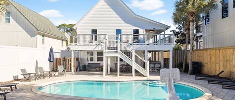 A two-story house with a pool, outdoor furniture, and a wooden fence.