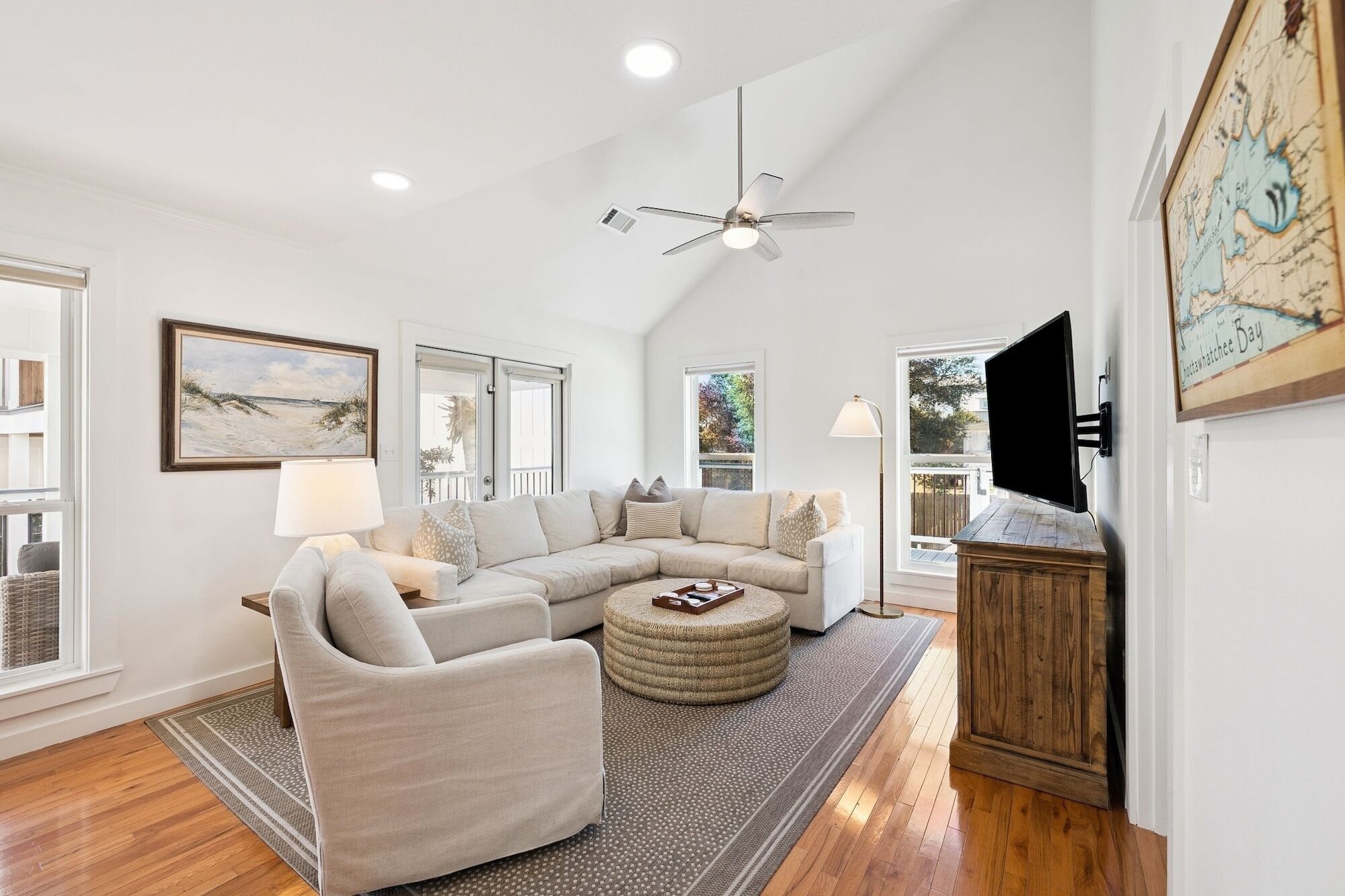 A spacious living room with a sectional sofa, a round ottoman, a ceiling fan, and a mounted TV.