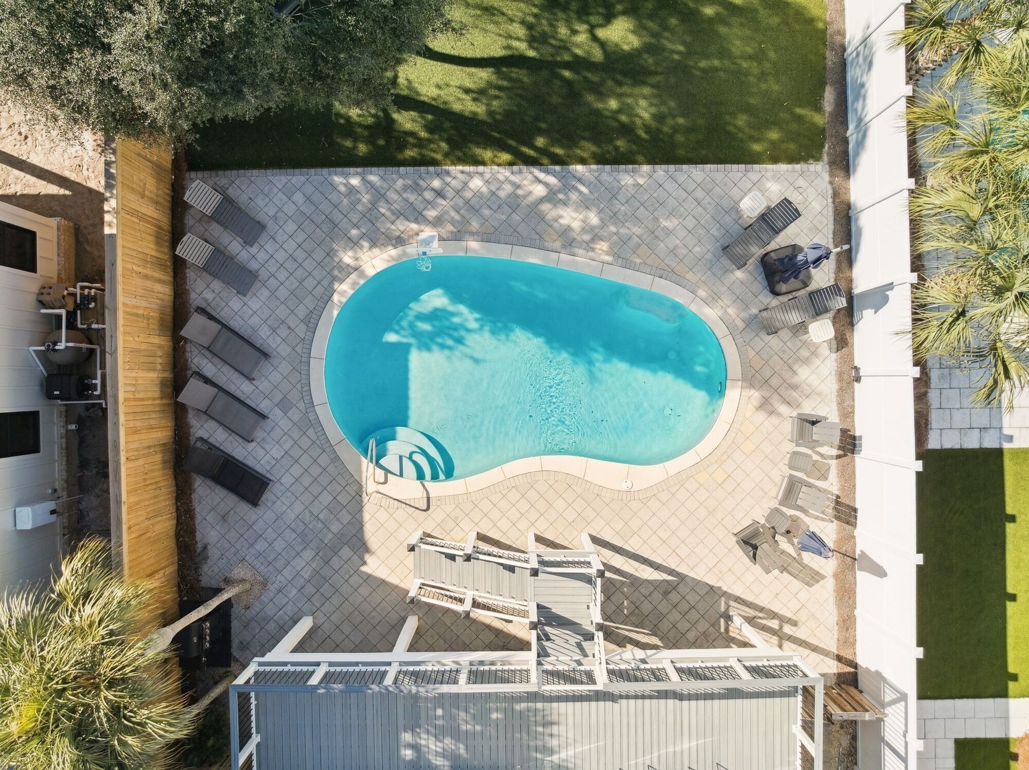 An aerial view of a swimming pool with a tiled deck, surrounded by lounge chairs and a covered area.