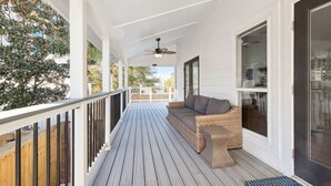 Een overdekte veranda met een houten terras, een rieten bank en een plafondventilator.