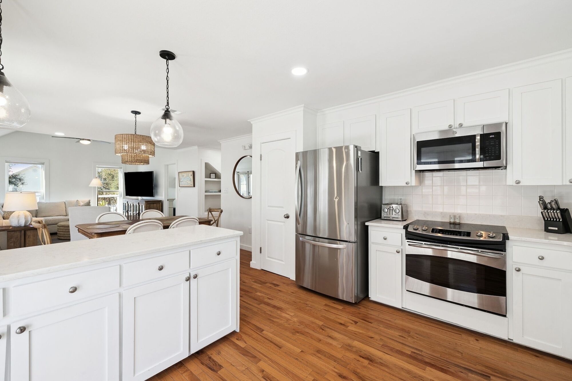 A modern kitchen with white cabinets, stainless steel appliances, and a wooden floor.
