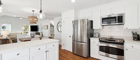 A modern kitchen with white cabinets, stainless steel appliances, and a wooden floor.