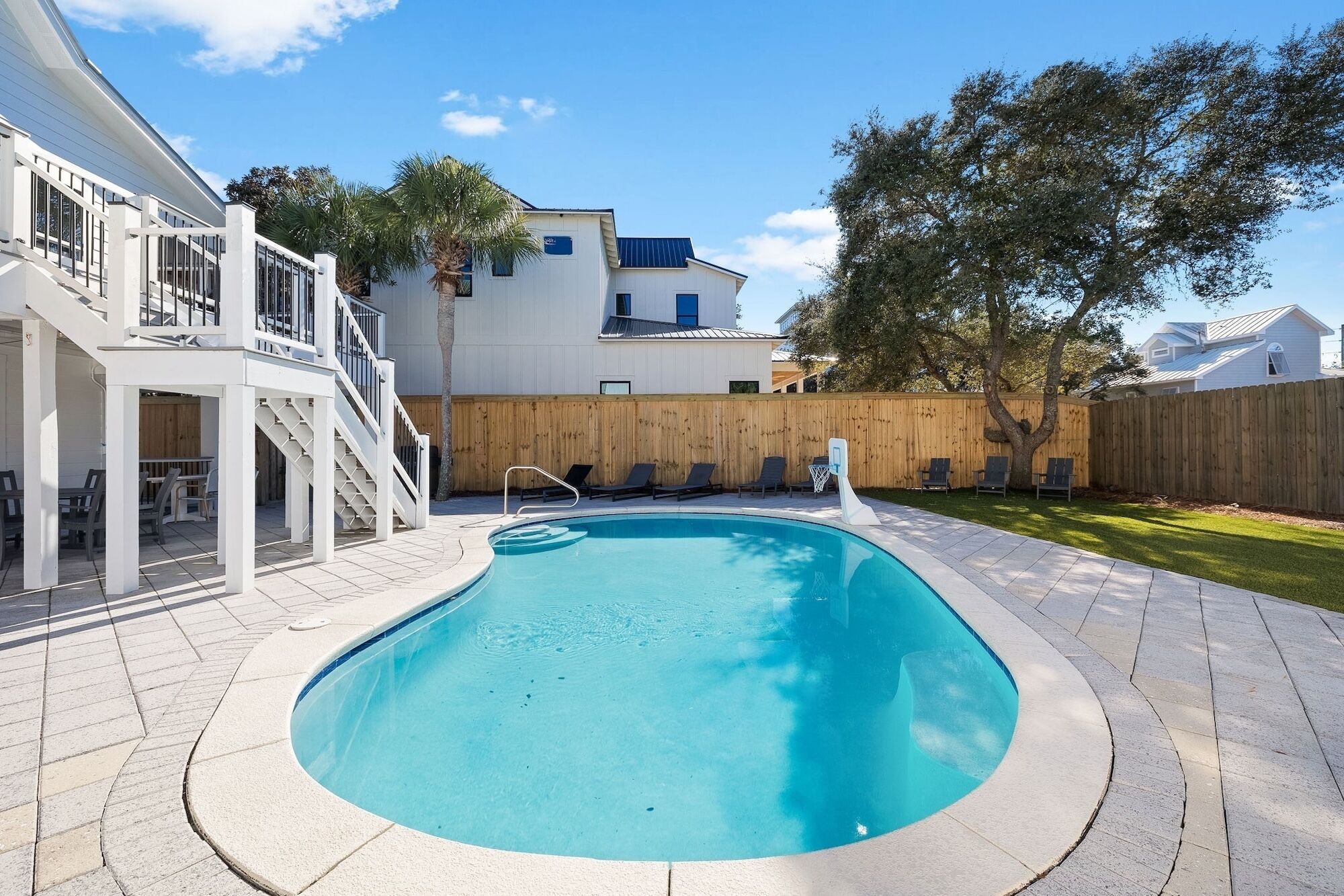 Ein Swimmingpool mit einer Holzterrasse und ein weißes Gebäude mit Balkon im Hintergrund.