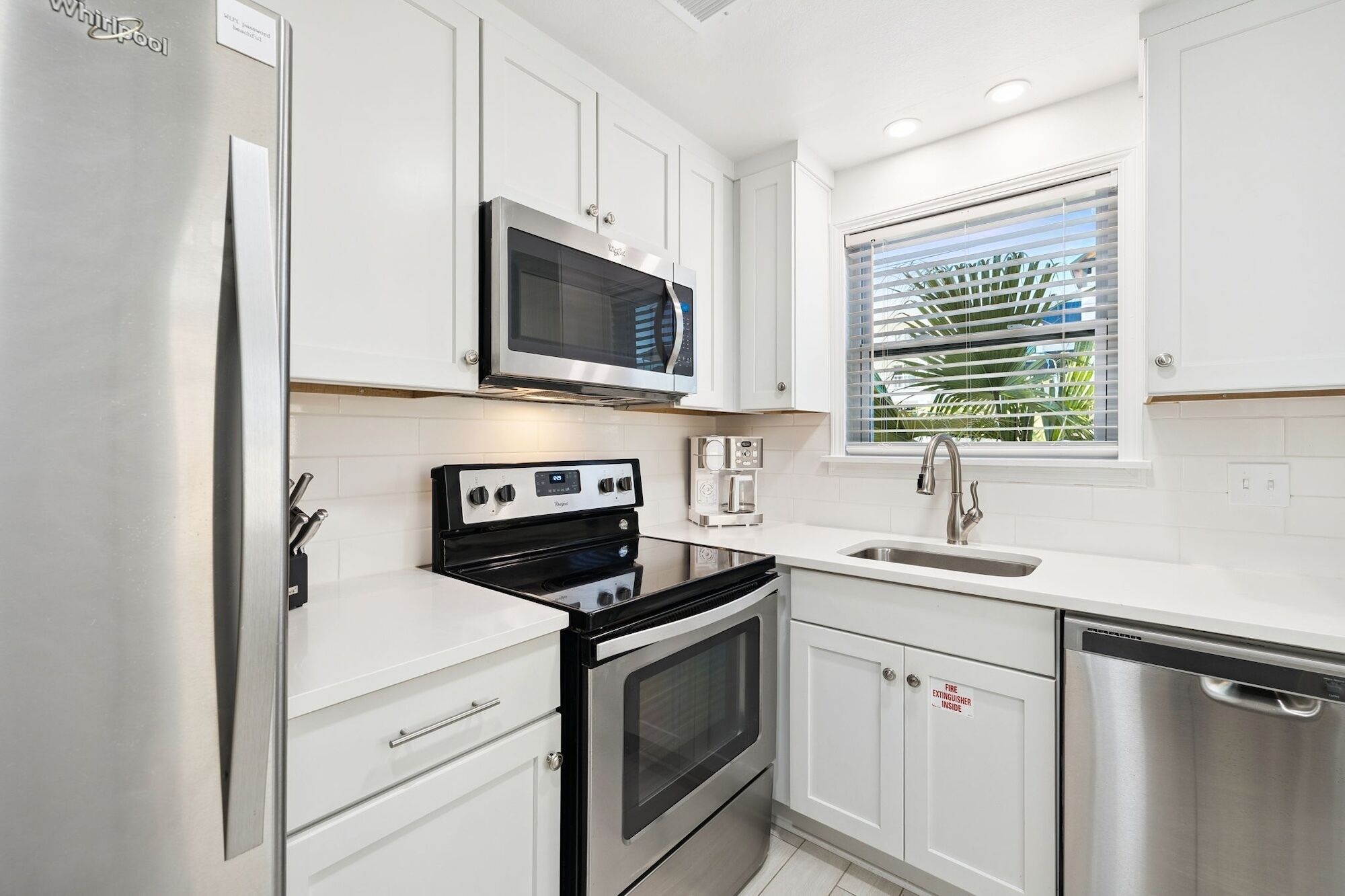 A modern kitchen with white cabinetry, a stainless steel refrigerator, a microwave, a stove, a coffee maker, and a dishwasher.
