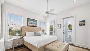 Une chambre à coucher comprenant un lit, une table de chevet, une lampe, un ventilateur de plafond et une fenêtre avec des stores.