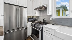 Une cuisine moderne dotée d’appareils électroménagers en acier inoxydable, de meubles blancs et offrant une vue sur une maison par une fenêtre.