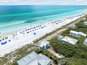 A beach with white sand, blue umbrellas, and a few buildings. - Rooftop Gulf Views & Private Pool (Santa Rosa Beach)