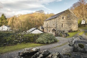 A stone building with a gravel path leading to it, surrounded by greenery and trees. - 1 Force Mill Barn | Ridgestone (Satterthwaite)