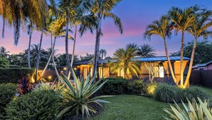 Ein modernes Haus mit einem gepflegten Garten, einschließlich Palmen und verschiedenen Sträuchern.