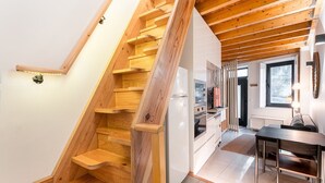Un escalier en bois mène à une cuisine dotée de meubles blancs et à un coin repas avec une table et des chaises.