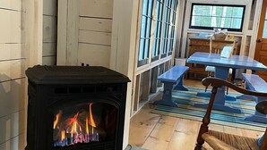 Ett mysigt rum med en vedeldad kamin, träväggar, en gungstol och ett matbord.