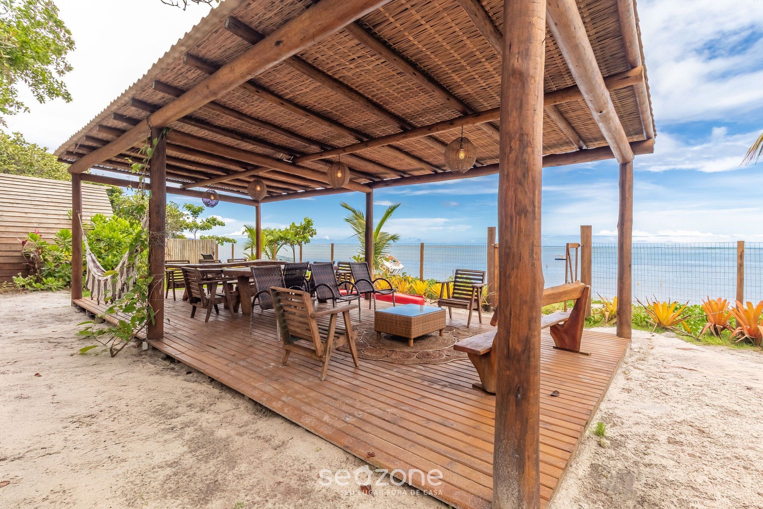 Una terraza de madera con mobiliario exterior, un espacio de estar cubierto y vista al océano.