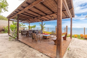 A wooden deck with outdoor furniture, a covered seating area, and a view of the ocean. - Beachfront Cabins in Bahia – OTX (Porto Seguro)