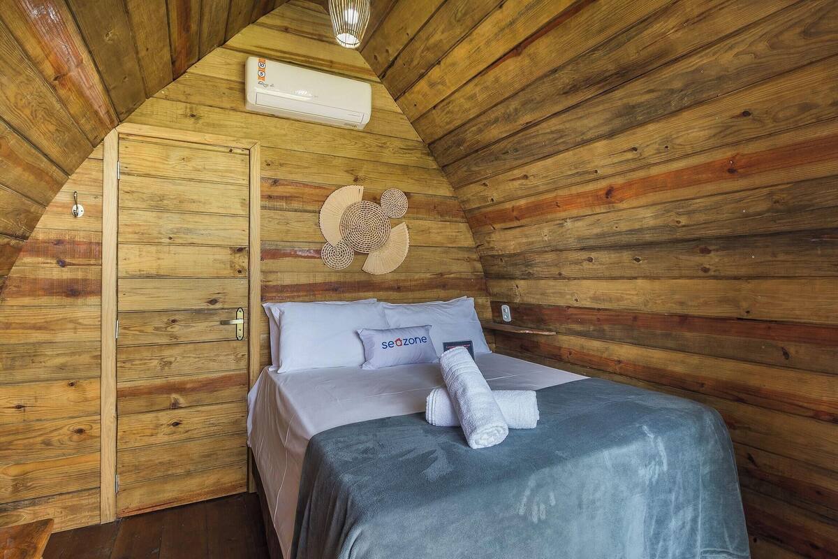A cozy wooden cabin room with a bed, a wall-mounted air conditioner, and a decorative wall hanging.